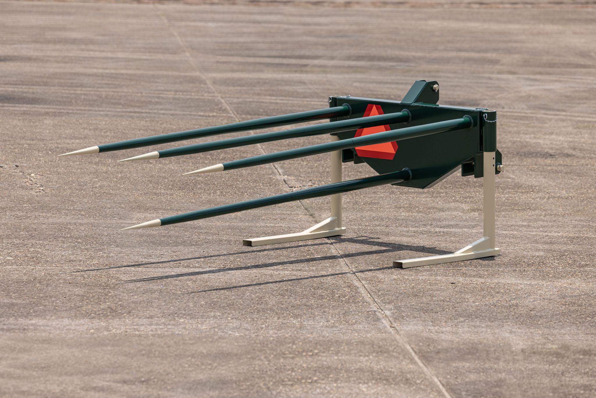 agriculture implement with 4 spikes on front sitting on concrete airport tarmac.